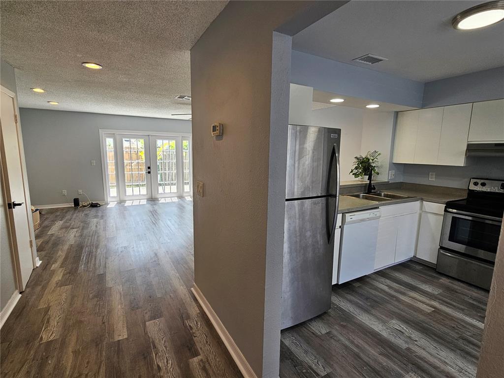 A kitchen with stainless steel appliances and white cabinets opens into a living area — 13817 STONE MILL WAY, TAMPA, FL
