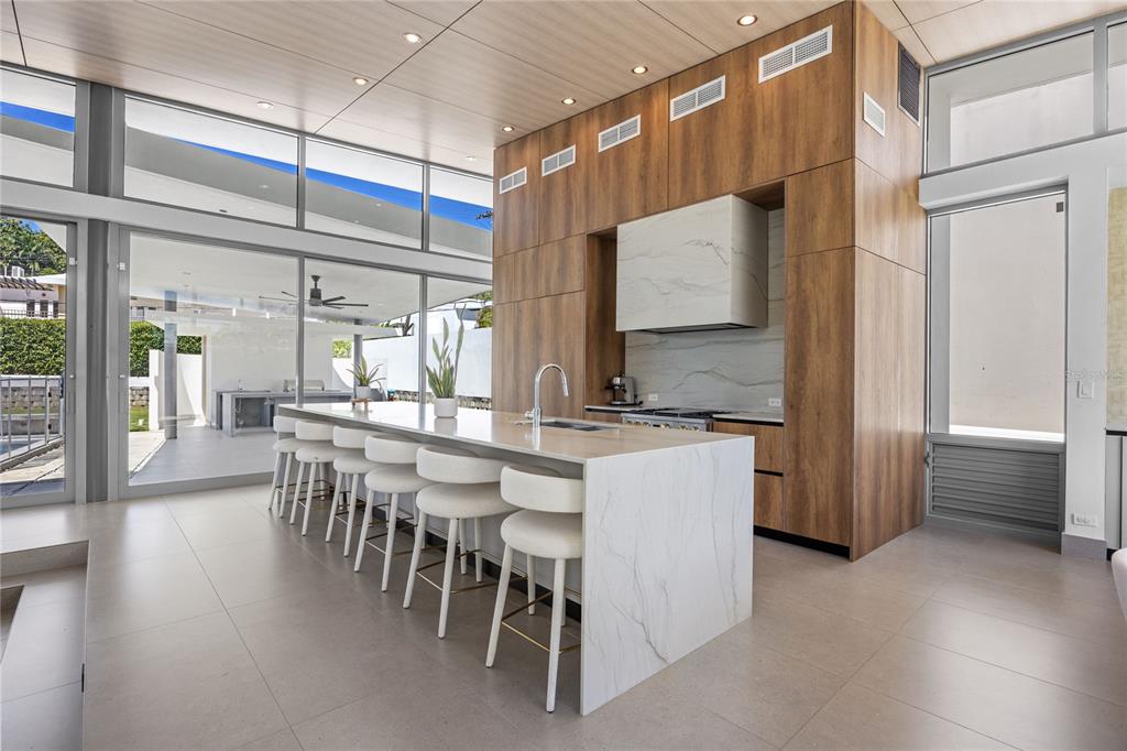 A modern kitchen features a large marble waterfall island, wood cabinetry, and floor-to-ceiling windows — A5 MEADOW LANE, GUAYNABO, PR
