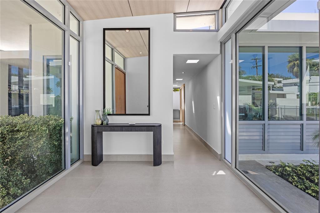 A modern entryway features a dark console table, a tall mirror, and glass walls overlooking greenery — A5 MEADOW LANE, GUAYNABO, PR