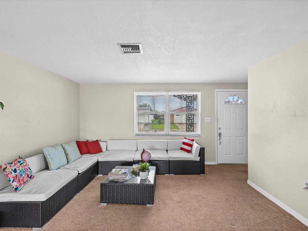 A living room features beige walls, brown carpeting, a large sectional sofa, and a front door — 1023 VIKING DRIVE, HOLIDAY, FL