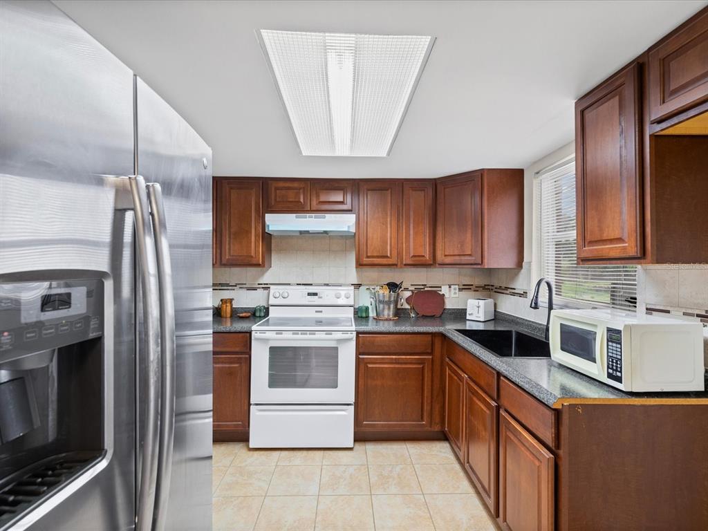 A kitchen with wood cabinets, stainless steel refrigerator, white stove, and dark countertops — 1023 VIKING DRIVE, HOLIDAY, FL