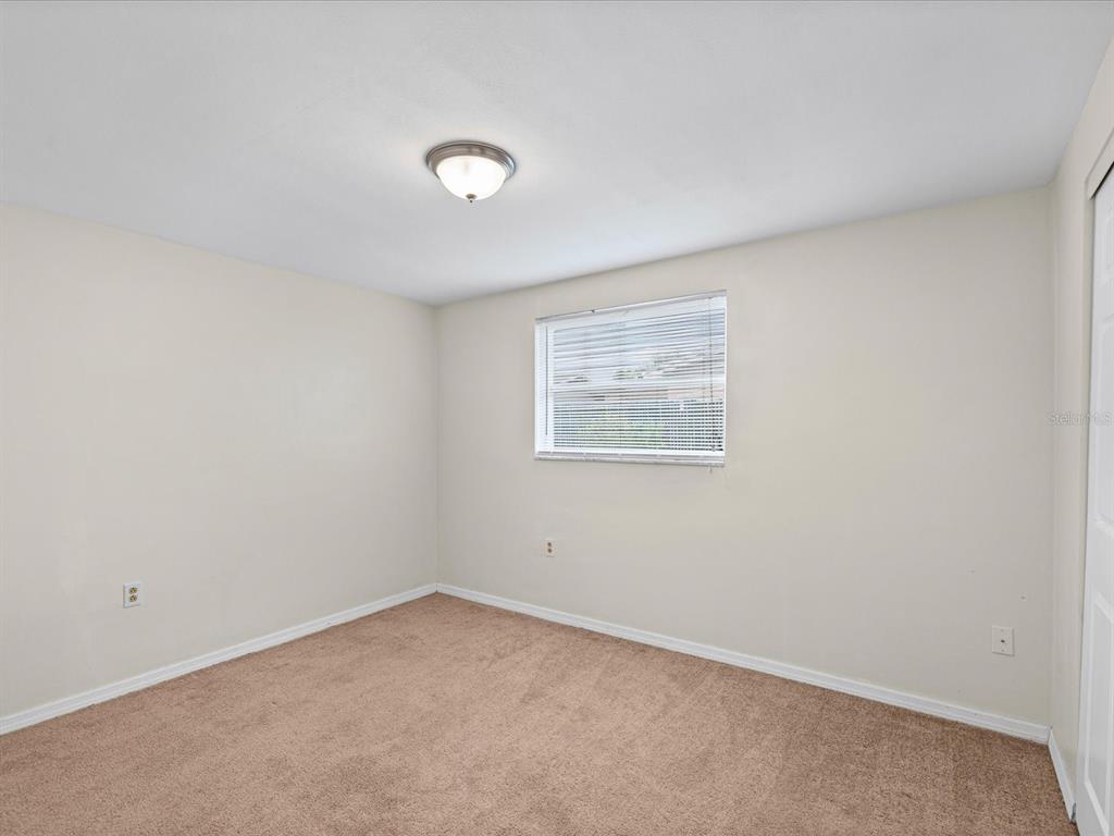 An empty bedroom features beige walls, brown carpeting, a ceiling light, and a single window — 1023 VIKING DRIVE, HOLIDAY, FL
