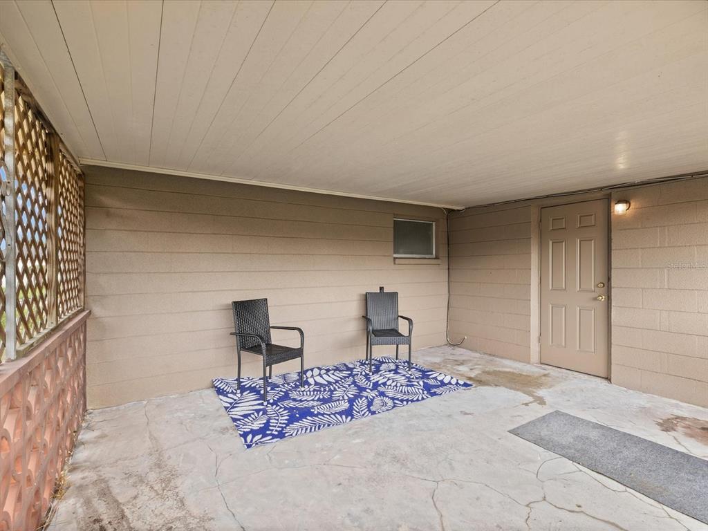 A covered concrete patio features two black chairs on a blue patterned rug — 1023 VIKING DRIVE, HOLIDAY, FL