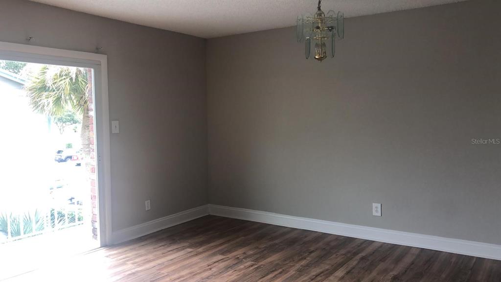 An empty room features gray walls, wood-look flooring, a chandelier, and a sliding glass door — 3035 GEORGE MASON AVENUE UNIT D20, WINTER PARK, FL