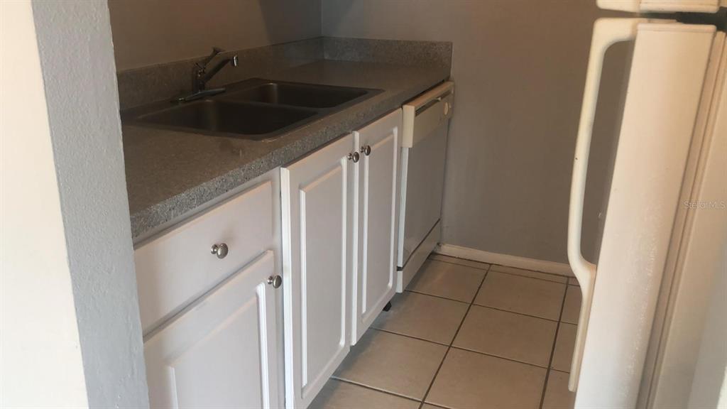 A kitchen features white cabinets, a double-basin sink, a dishwasher, and light-colored tile flooring — 3035 GEORGE MASON AVENUE UNIT D20, WINTER PARK, FL