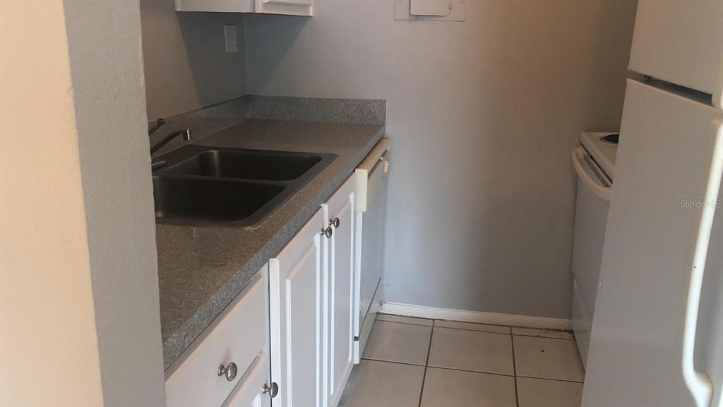 A small kitchen features white cabinets, a double sink, gray countertops, and white appliances — 3035 GEORGE MASON AVENUE UNIT D20, WINTER PARK, FL