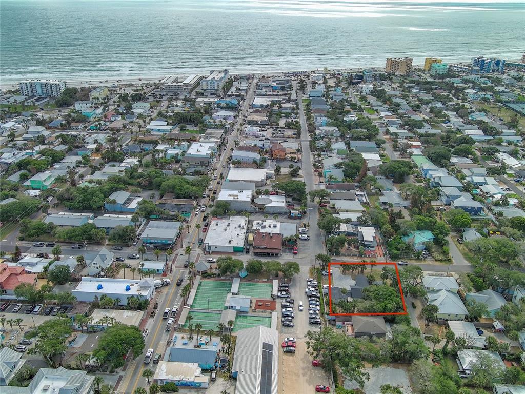 An aerial view shows a coastal town with a red-outlined property near tennis courts — 200 S PINE STREET, NEW SMYRNA BEACH, FL
