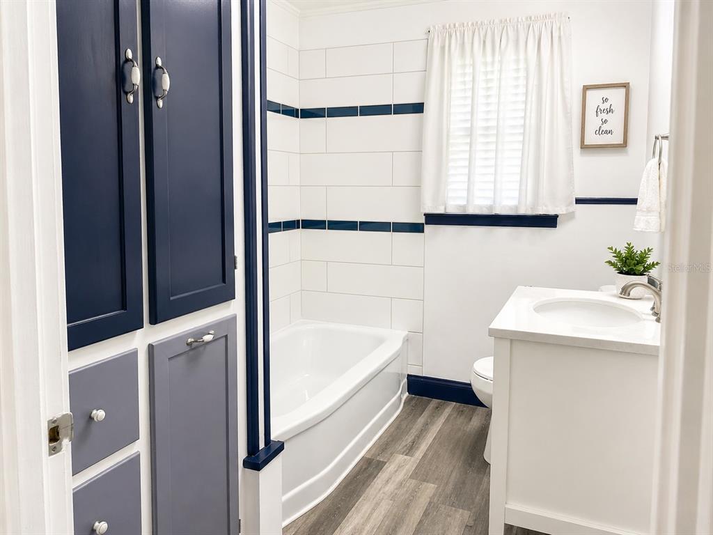 A bathroom features a white vanity, a bathtub with blue-accented tile, and navy blue cabinets — 200 S PINE STREET, NEW SMYRNA BEACH, FL
