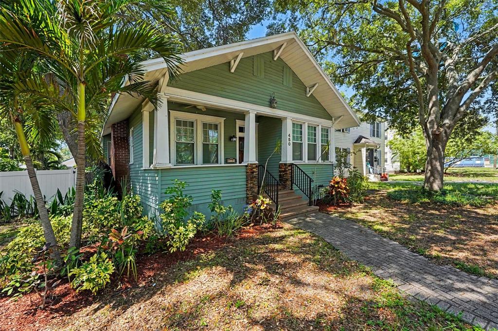 A green bungalow with a front porch, stone accents, and a brick walkway — 450 13TH AVENUE N, ST PETERSBURG, FL