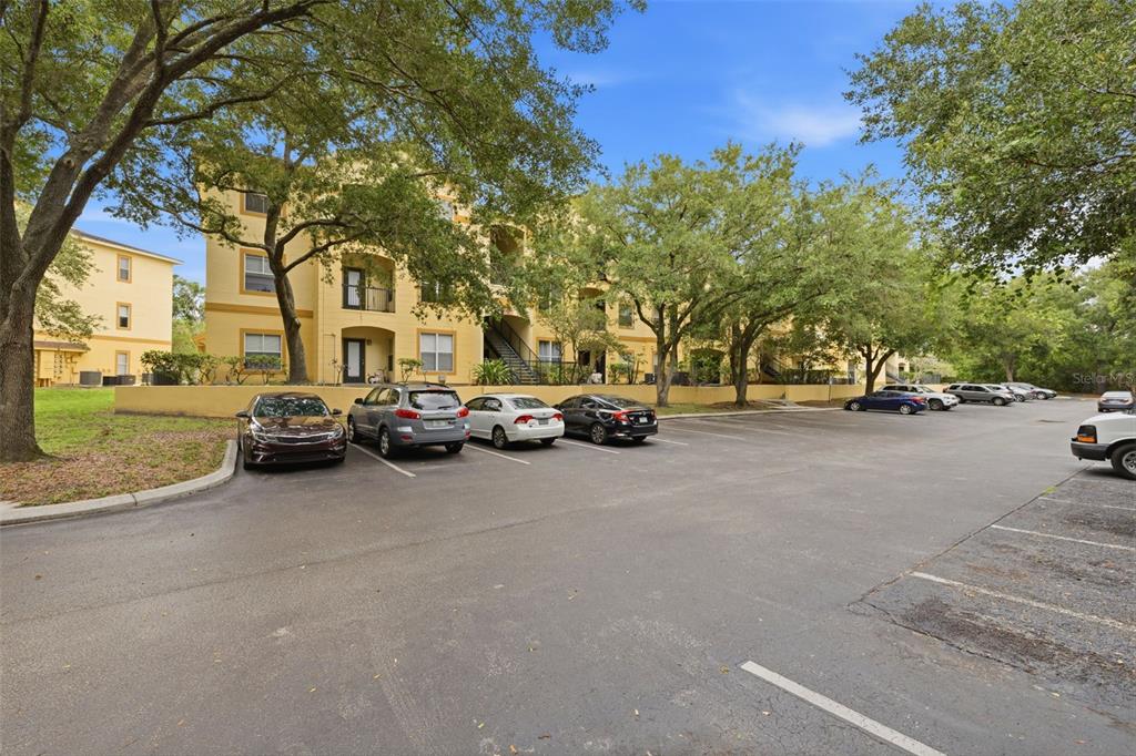 A multi-story yellow apartment building sits behind a paved parking lot with several parked cars — 5612 PINNACLE HEIGHTS CIRCLE UNIT 312, TAMPA, FL