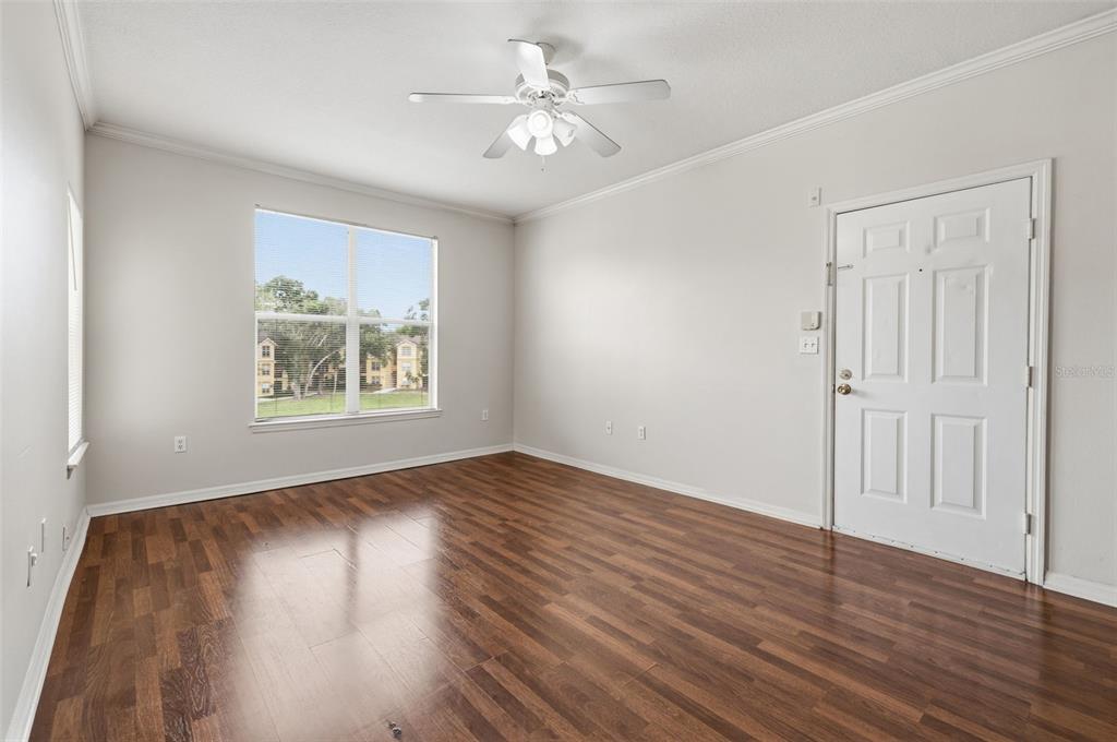 An empty room features wood-look flooring, white walls, a ceiling fan, and a front door — 5612 PINNACLE HEIGHTS CIRCLE UNIT 312, TAMPA, FL