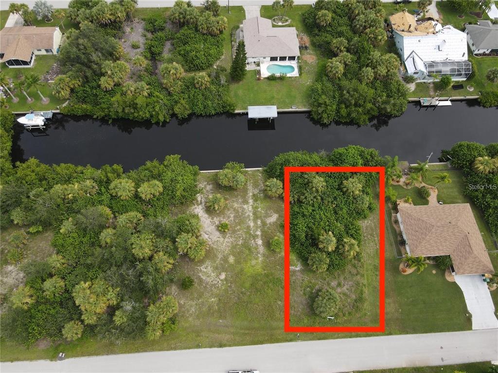 An aerial view shows a vacant, wooded residential lot outlined in red next to a canal — 18694 ARAPAHOE CIRCLE, PORT CHARLOTTE, FL