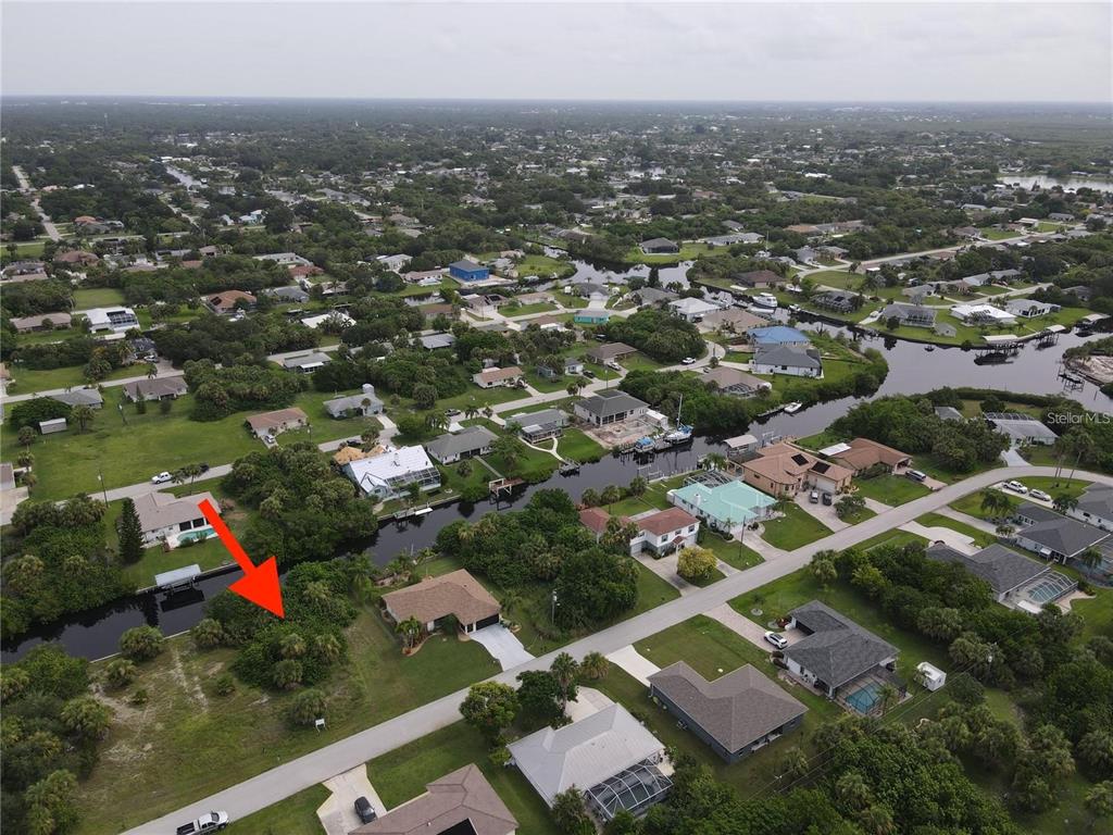 An aerial view shows a vacant, tree-covered waterfront lot next to a residential house — 18694 ARAPAHOE CIRCLE, PORT CHARLOTTE, FL