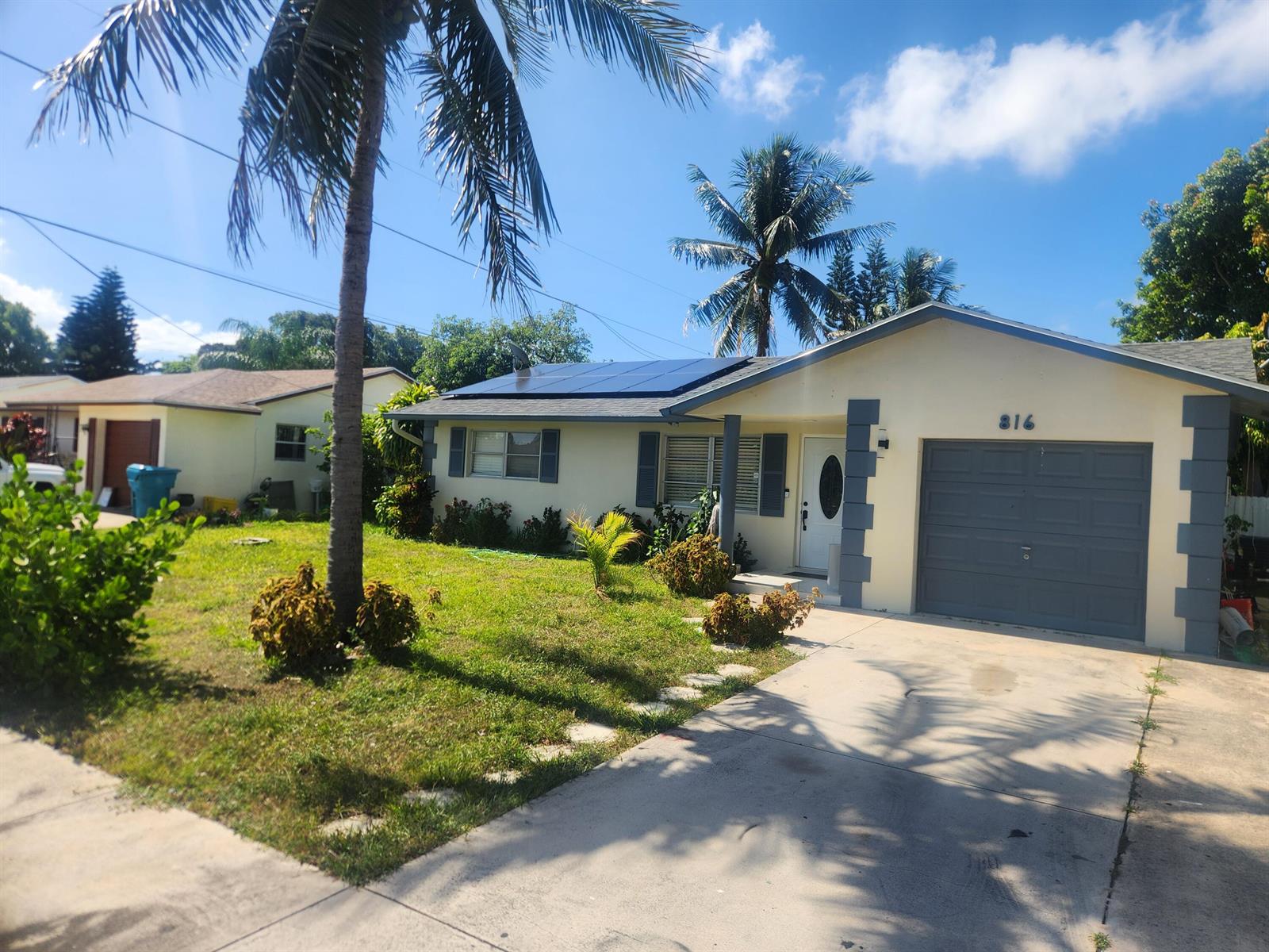 A single-story house with a gray garage, solar panels on the roof, and palm trees — 816 NW 8th Avenue, Boynton Beach FL 33426, BOYNTON BEACH, FL