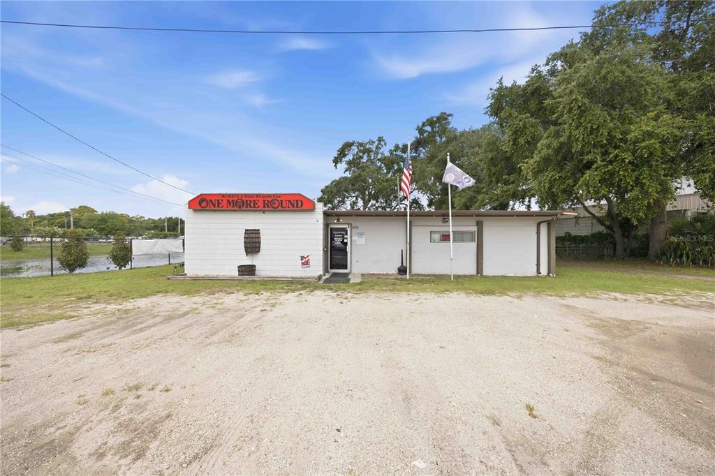 A single-story commercial building with a gravel parking lot and an American flag — 404 EAKER STREET, AUBURNDALE, FL