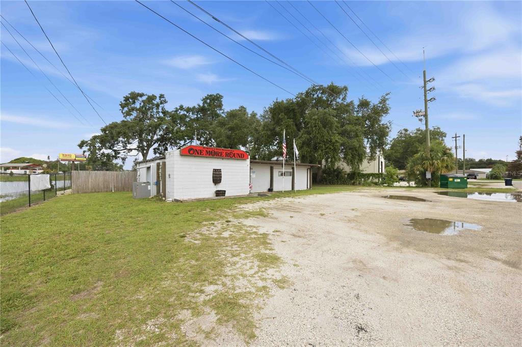 A white, single-story commercial building with a gravel parking lot and large trees — 404 EAKER STREET, AUBURNDALE, FL