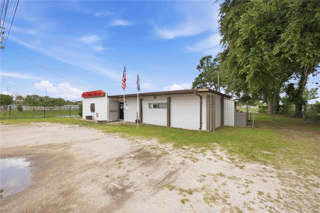 A single-story commercial building with a gravel parking lot and two flagpoles in front — 404 EAKER STREET, AUBURNDALE, FL