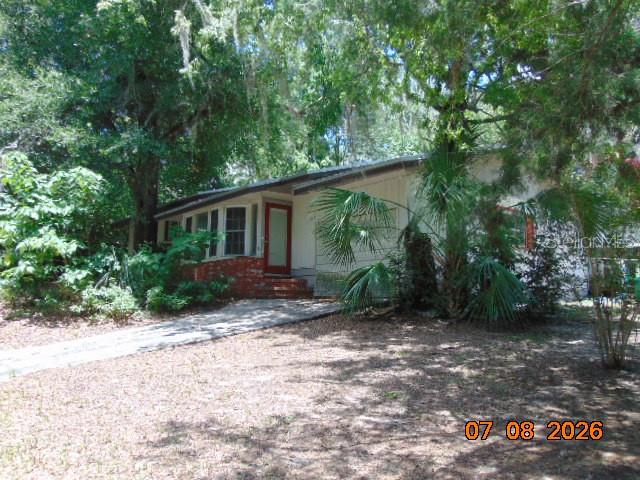 A single-story house with a brick accent wall, a red front door, and surrounding trees — 2105 NW 16TH TERRACE NW, GAINESVILLE, FL