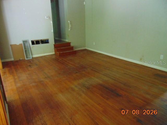 An empty room with hardwood floors, a small set of stairs, and a wall opening — 2105 NW 16TH TERRACE NW, GAINESVILLE, FL