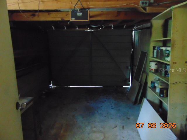 A dimly lit garage features a closed sectional door, exposed ceiling joists, and wooden shelving — 2105 NW 16TH TERRACE NW, GAINESVILLE, FL