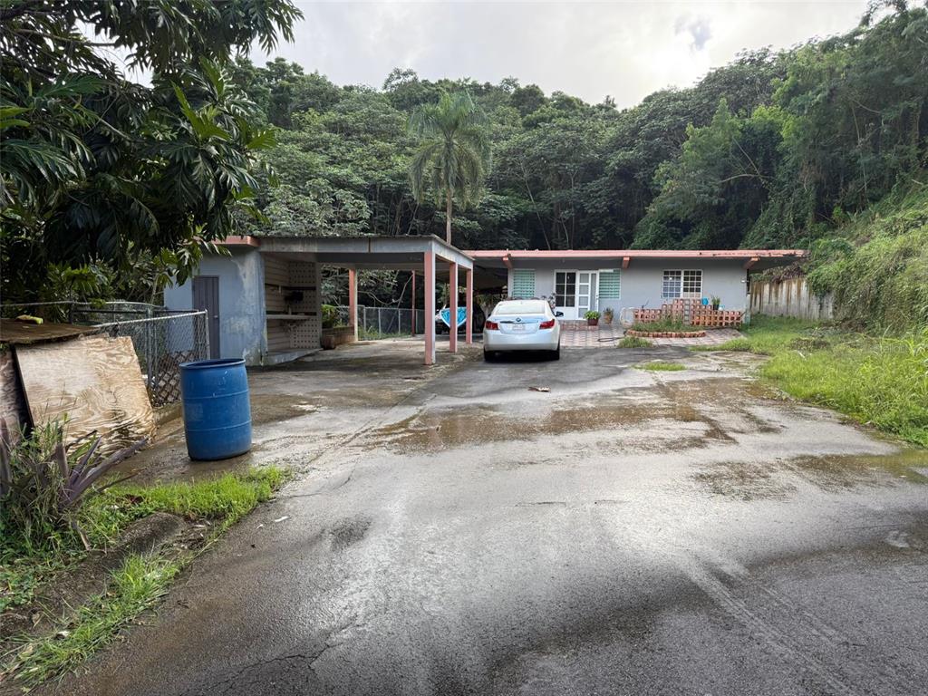 A single-story house with a carport and a large paved driveway sits against a hillside — Carr 925 KM 4.9 BO. JUNQUITO, HUMACAO, PR