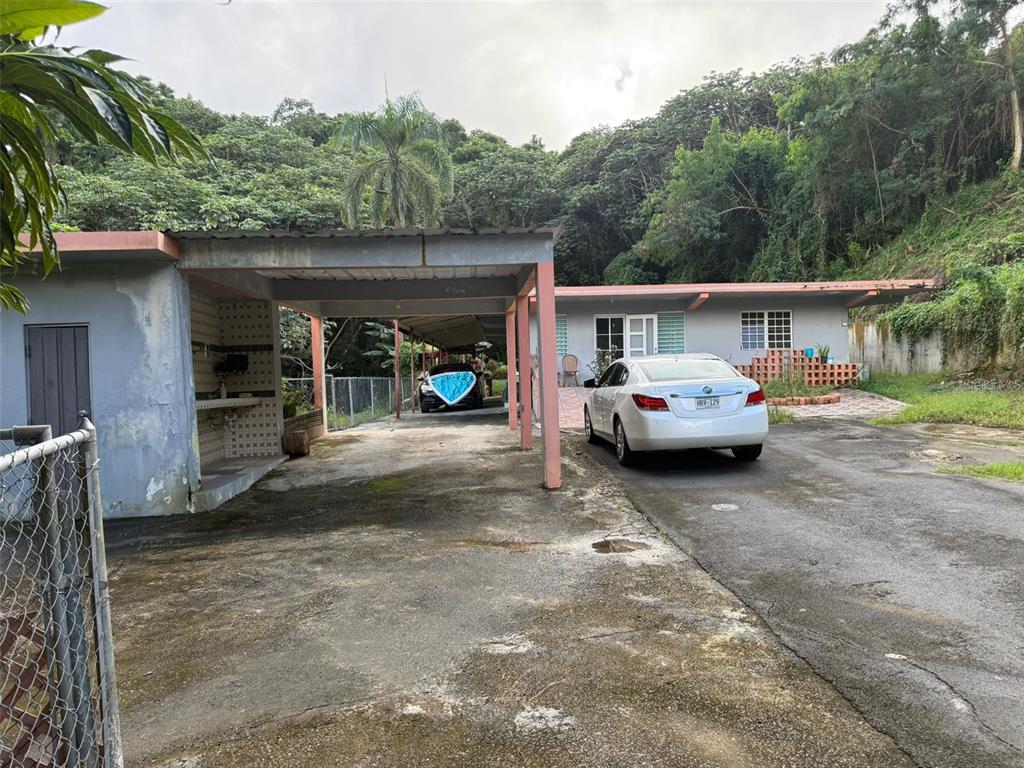 A single-story house with a carport, a white sedan, and a wooded hillside background — Carr 925 KM 4.9 BO. JUNQUITO, HUMACAO, PR