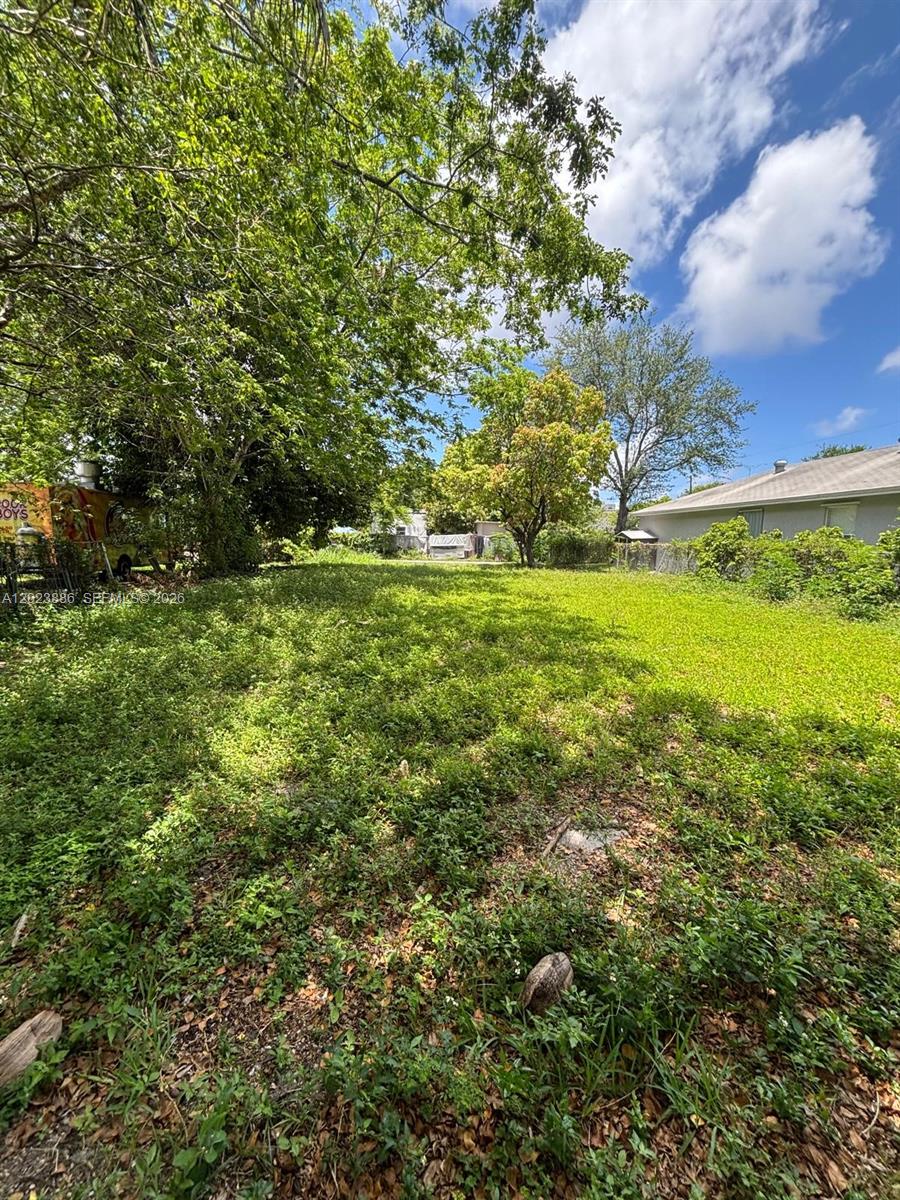 A grassy, overgrown vacant lot is bordered by trees and a neighboring house — 665 NW 43rd St, Miami FL 33127, MIAMI, FL
