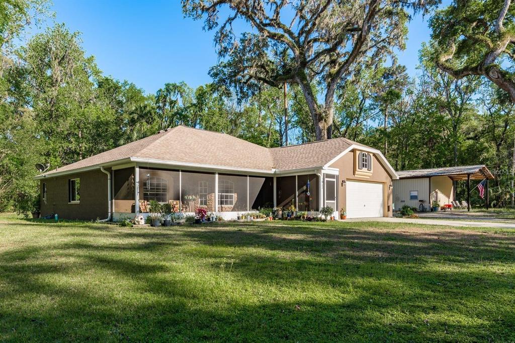 A single-story house with a large screened-in porch and an attached garage sits on a lawn — 7182 GRIFFIN ROAD, BROOKSVILLE, FL