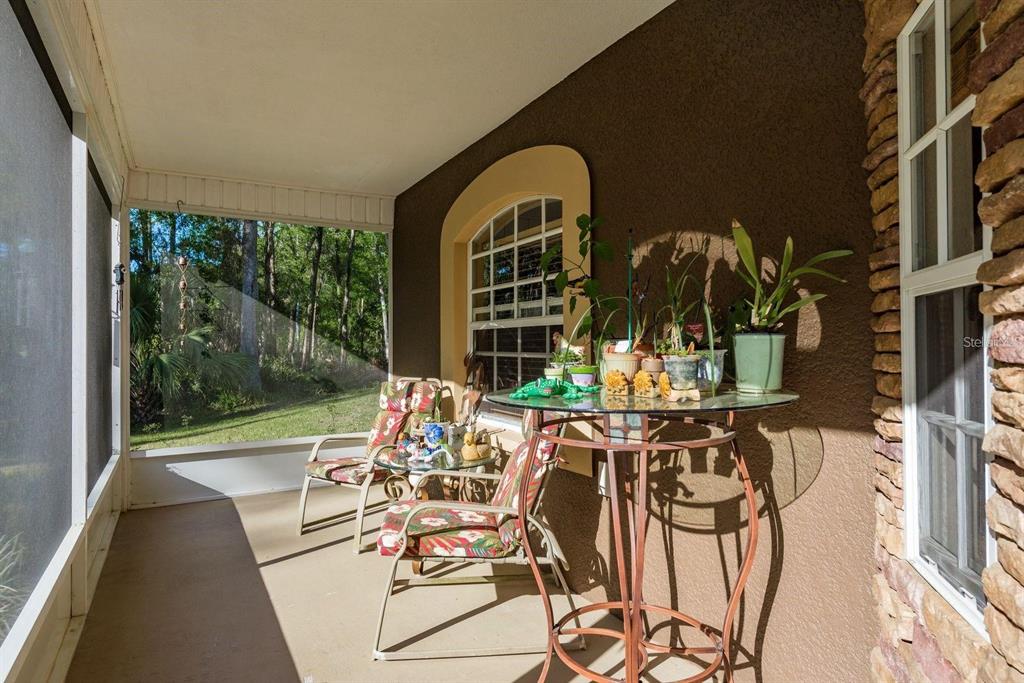 A screened-in porch features a glass-topped table, two floral chairs, and a view of trees — 7182 GRIFFIN ROAD, BROOKSVILLE, FL