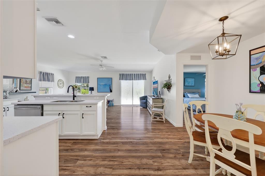 An open-concept kitchen and dining area features white cabinetry, wood-look flooring, and a pendant light — 25174 ALCAZAR DRIVE, PUNTA GORDA, FL