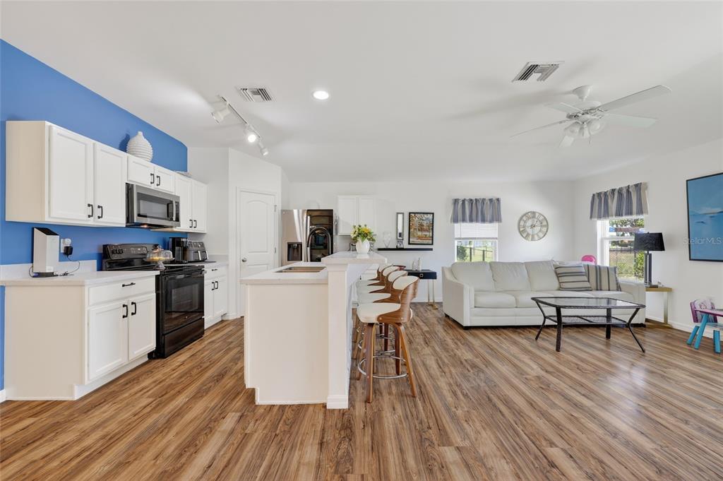 An open-concept kitchen and living area features white cabinetry, a blue accent wall, and wood-look flooring — 25174 ALCAZAR DRIVE, PUNTA GORDA, FL