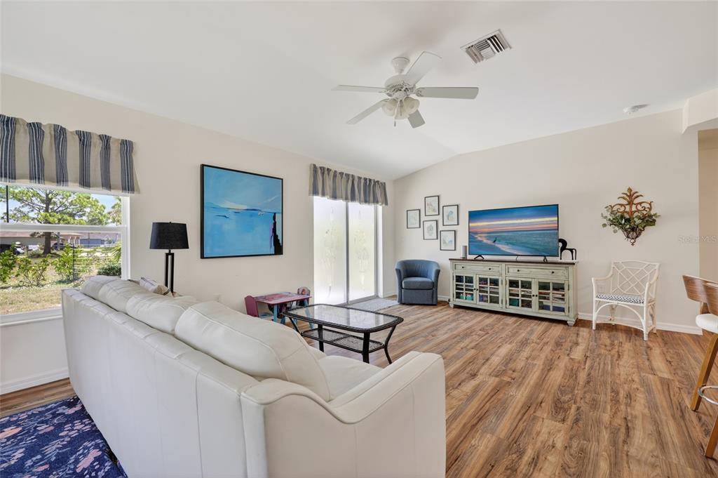 A living room features a white sofa, wood-look flooring, a ceiling fan, and a television — 25174 ALCAZAR DRIVE, PUNTA GORDA, FL