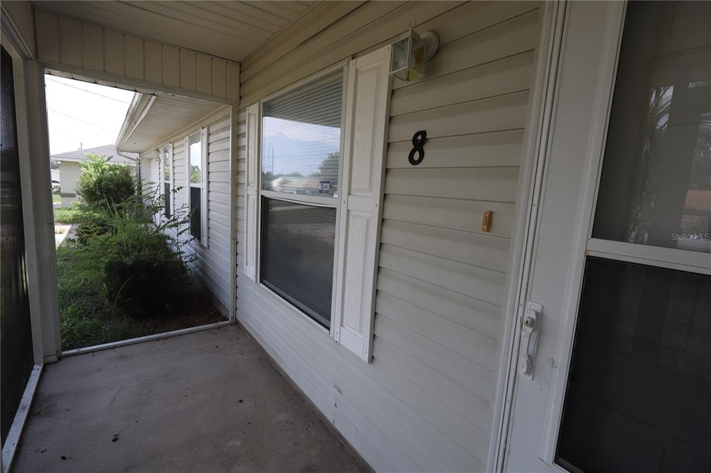 A covered concrete porch features light-colored vinyl siding, a window with shutters, and number eight — 8 HEMLOCK TERRACE, OCALA, FL