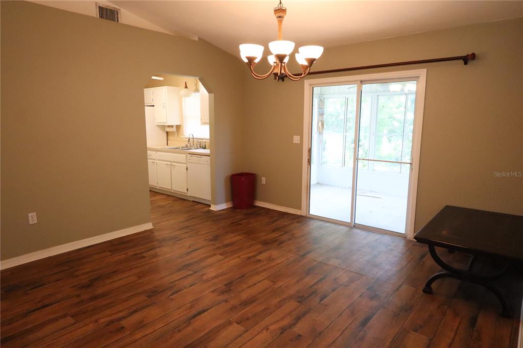 A dining room with wood-look flooring, a chandelier, and a sliding glass door to a porch — 8 HEMLOCK TERRACE, OCALA, FL
