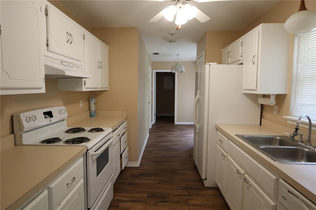 A galley kitchen features white cabinets, tan countertops, white appliances, and wood-look flooring — 8 HEMLOCK TERRACE, OCALA, FL