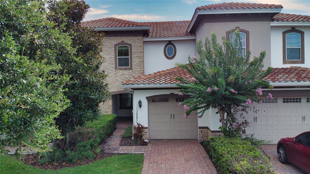 A two-story townhouse with a stone facade, tile roof, and a brick-paved driveway — 13880 ARCLID STREET, ORLANDO, FL