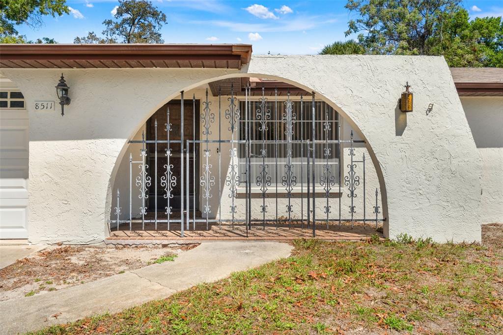 The exterior of a house features a white stucco wall with an arched wrought-iron gate — 8511 LONG BOAT LANE, HUDSON, FL
