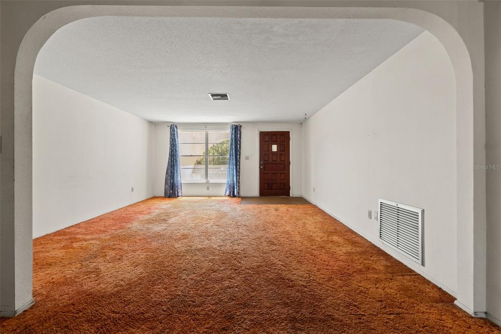 An empty living room features orange wall-to-wall carpeting, white walls, and a front entry door — 8511 LONG BOAT LANE, HUDSON, FL