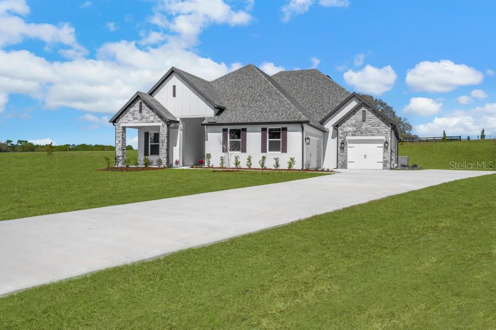 A single-story house with stone accents, white siding, and a concrete driveway on a grassy lot — 3845 SADDLE HILL TRAIL, FRUITLAND PARK, FL