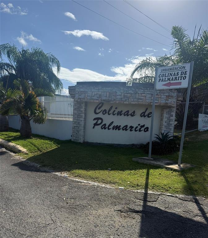 A stone entrance sign for the Colinas de Palmarito neighborhood stands beside a paved road — COLINAS DE PALMARITO, ARECIBO, PR