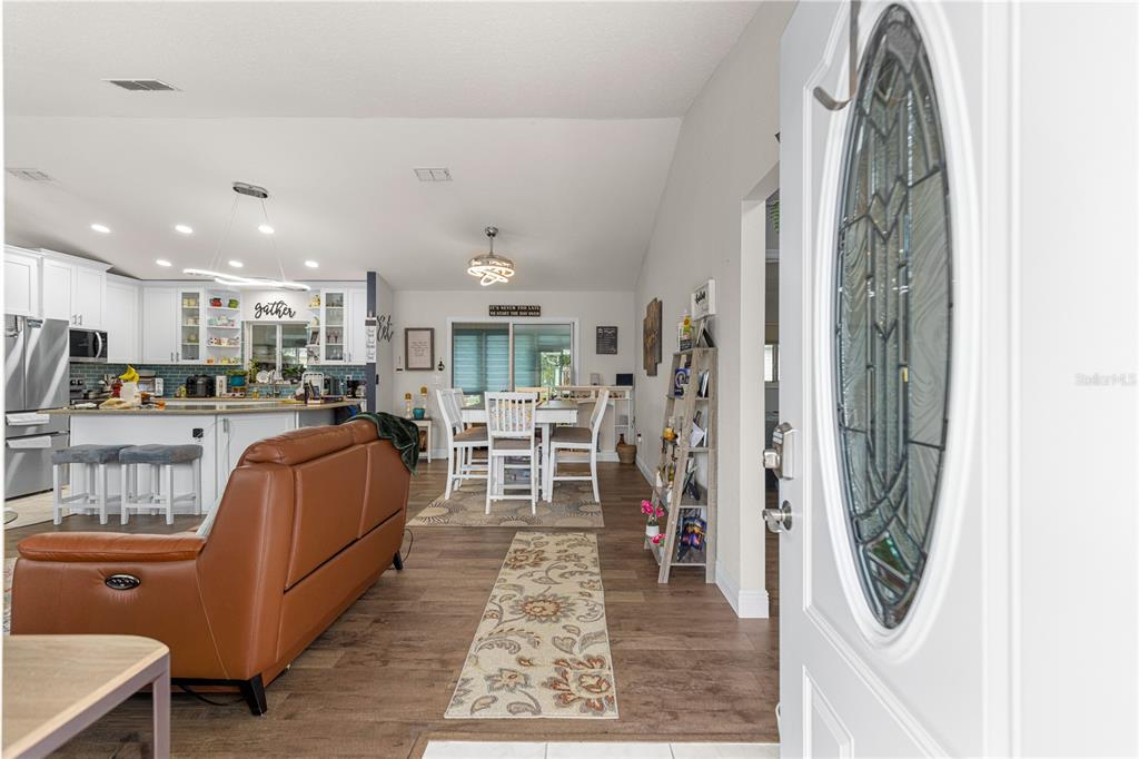 An open-concept living room and kitchen featuring wood-look flooring, a leather sofa, and dining area — 13834 SW 114TH AVENUE, DUNNELLON, FL