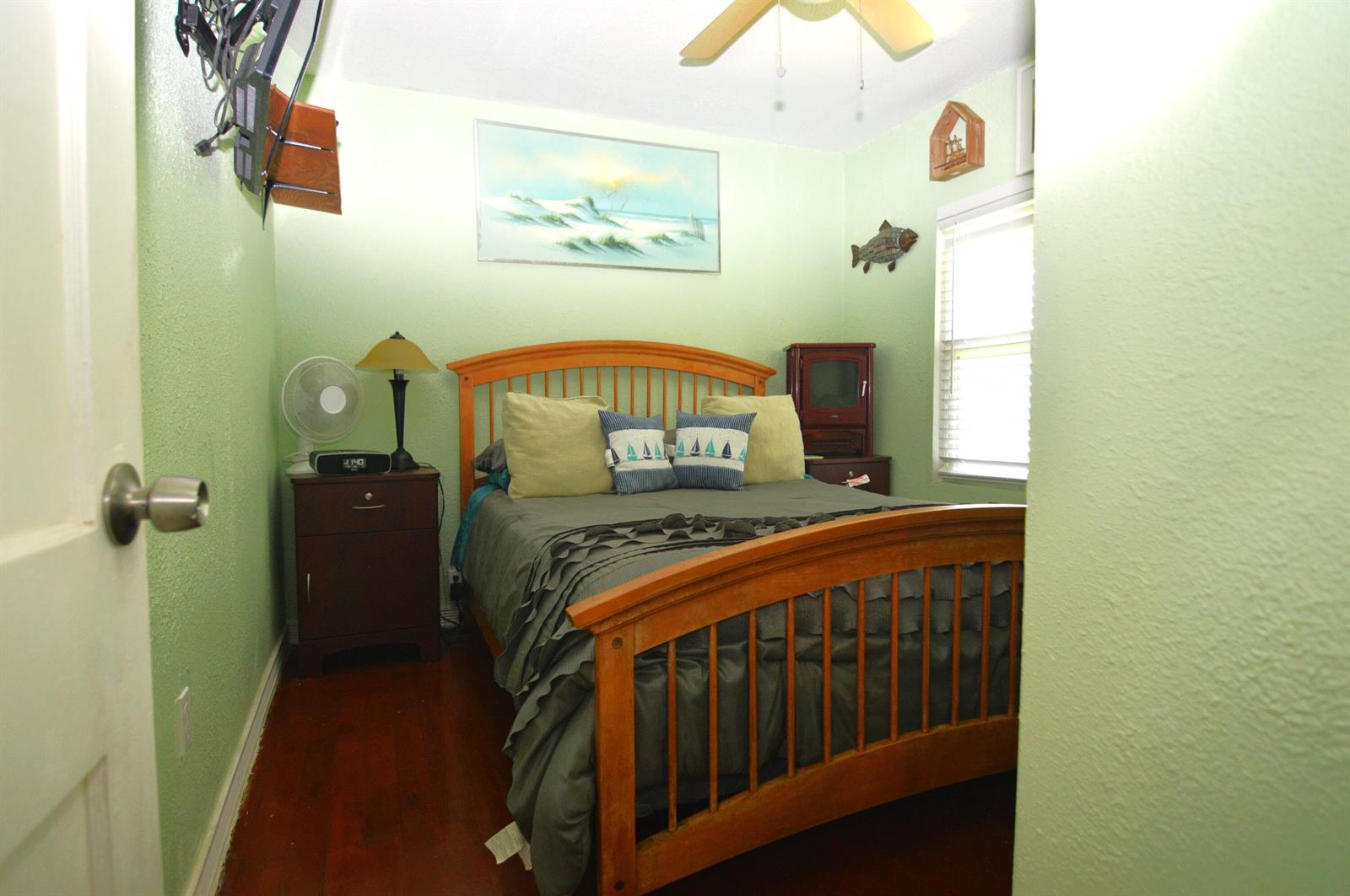 A bedroom with light green walls, a wooden bed frame, and dark wood flooring — 711 Cedar Place, Fort Pierce FL 34950, FORT PIERCE, FL
