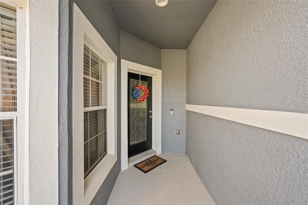 A covered entryway features a black front door with a decorative wreath and gray walls — 1562 TRAVERTINE TERRACE, SANFORD, FL