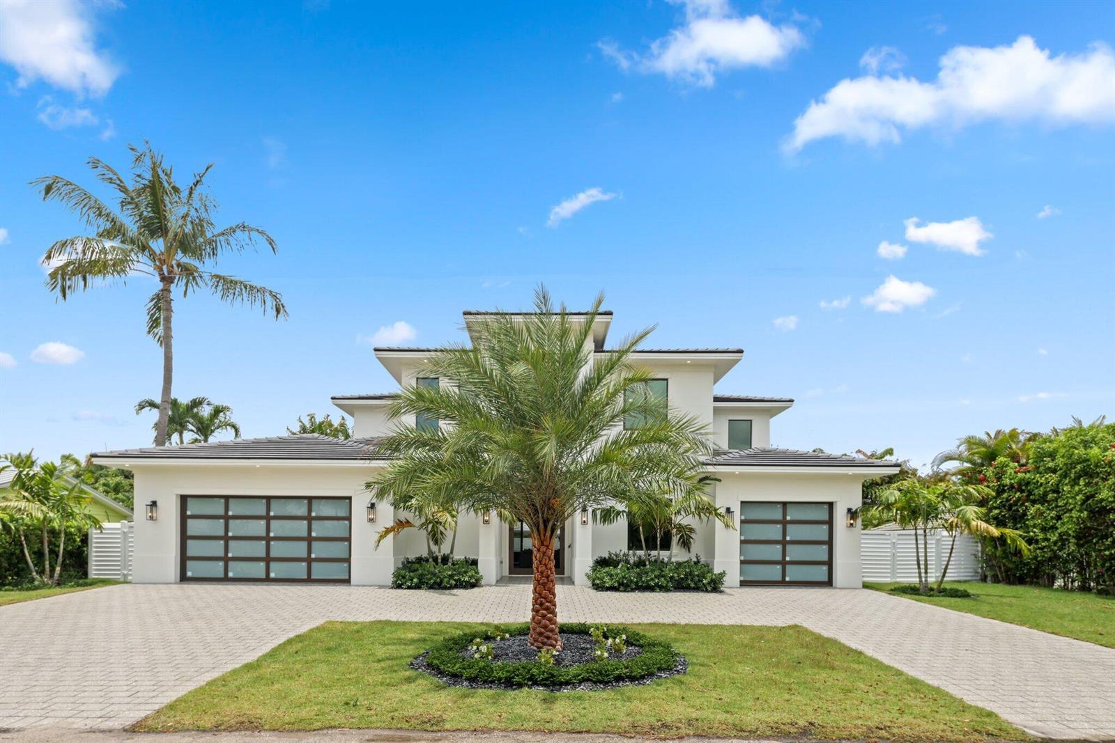 A two-story white house features a paved driveway, a central palm tree, and two garages — 1160 Emerald Drive, Riviera Beach FL 33404, RIVIERA BEACH, FL