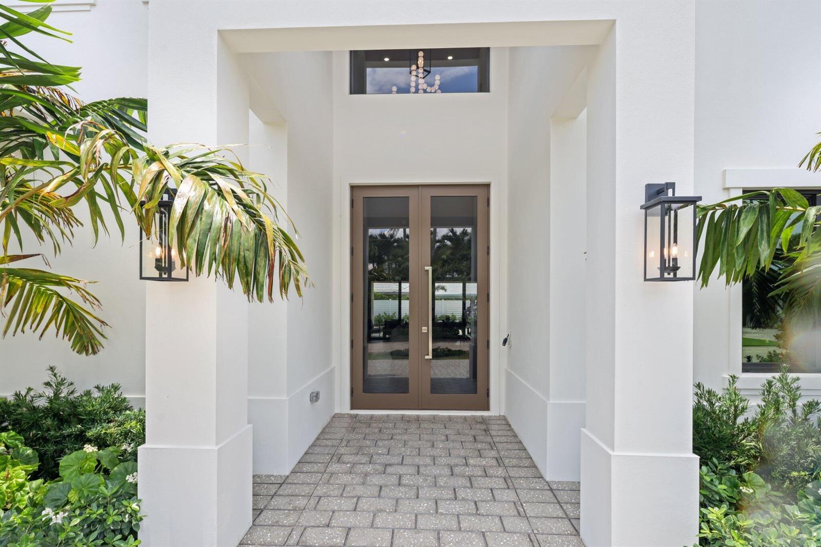 A modern white entryway features a double glass door, stone pavers, and two wall lanterns — 1160 Emerald Drive, Riviera Beach FL 33404, RIVIERA BEACH, FL