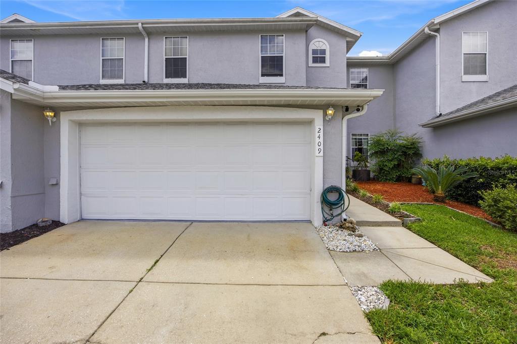 A two-story townhouse exterior features a white garage door, a concrete driveway, and landscaping — 2409 SW 20TH TERRACE, OCALA, FL