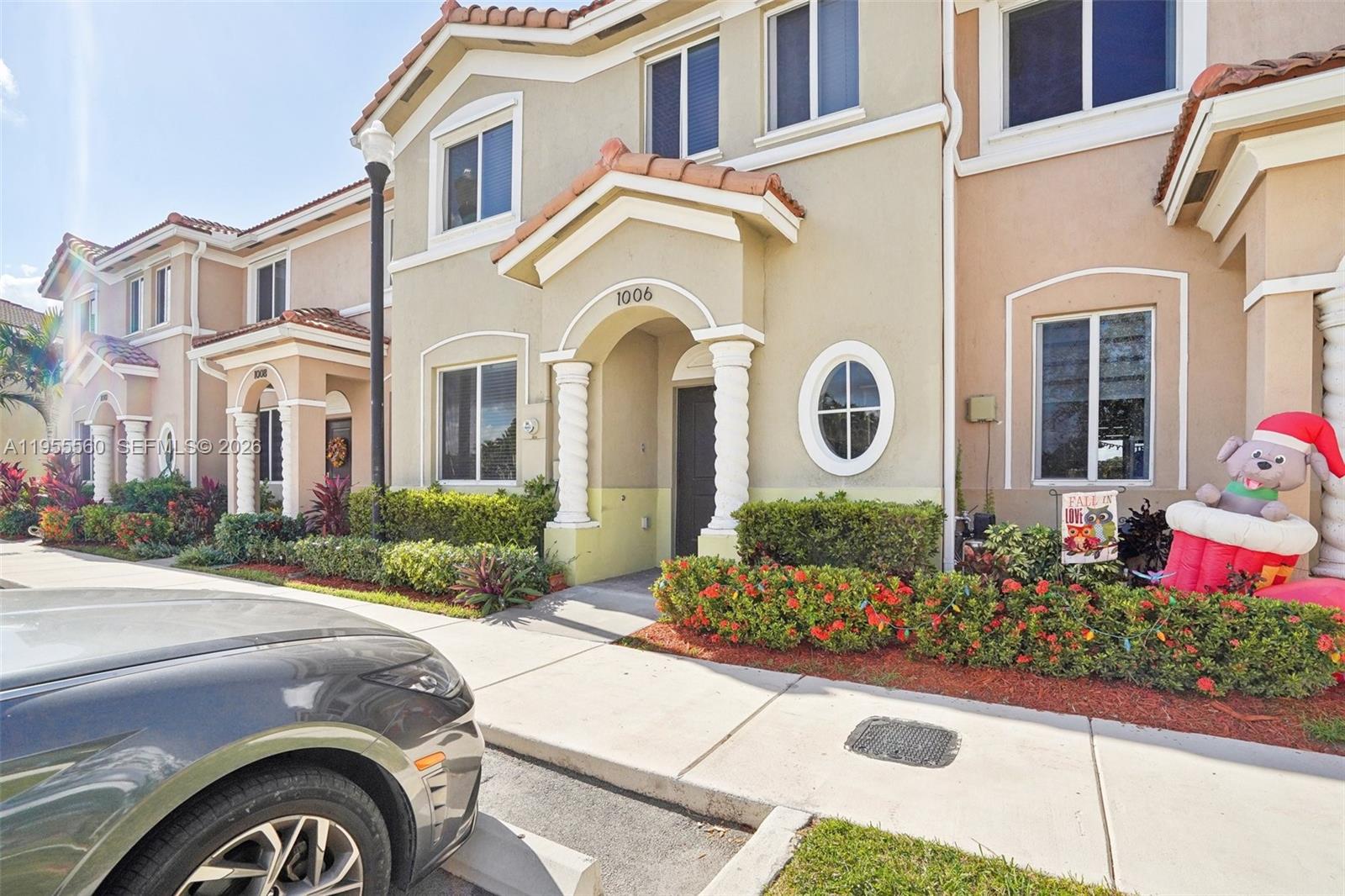 A two-story townhouse exterior features a beige facade, arched entryway, and a small front garden — 1006 SE 23rd Ave, Homestead FL 33035, HOMESTEAD, FL