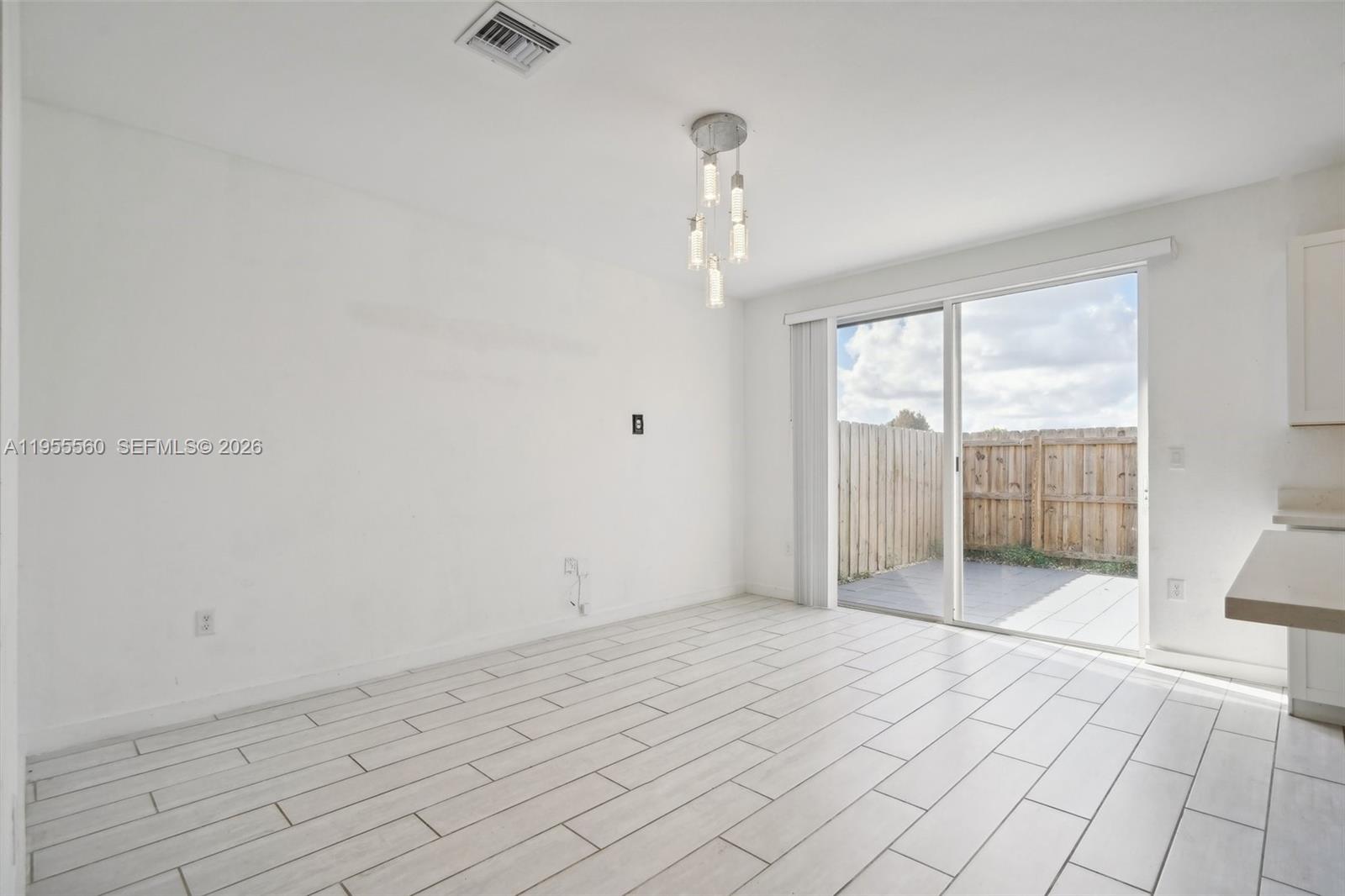 A bright dining area features white tile floors, a modern chandelier, and a sliding glass door — 1006 SE 23rd Ave, Homestead FL 33035, HOMESTEAD, FL