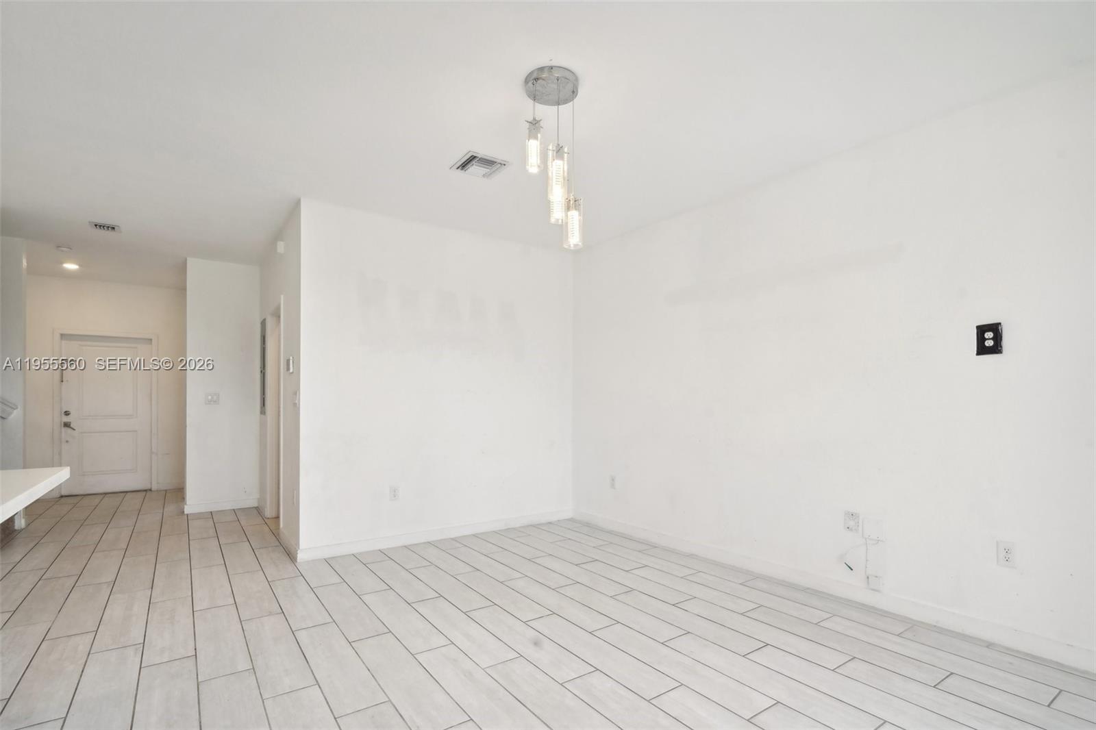 A minimalist room features white walls, light-colored tile flooring, and a modern pendant light fixture — 1006 SE 23rd Ave, Homestead FL 33035, HOMESTEAD, FL