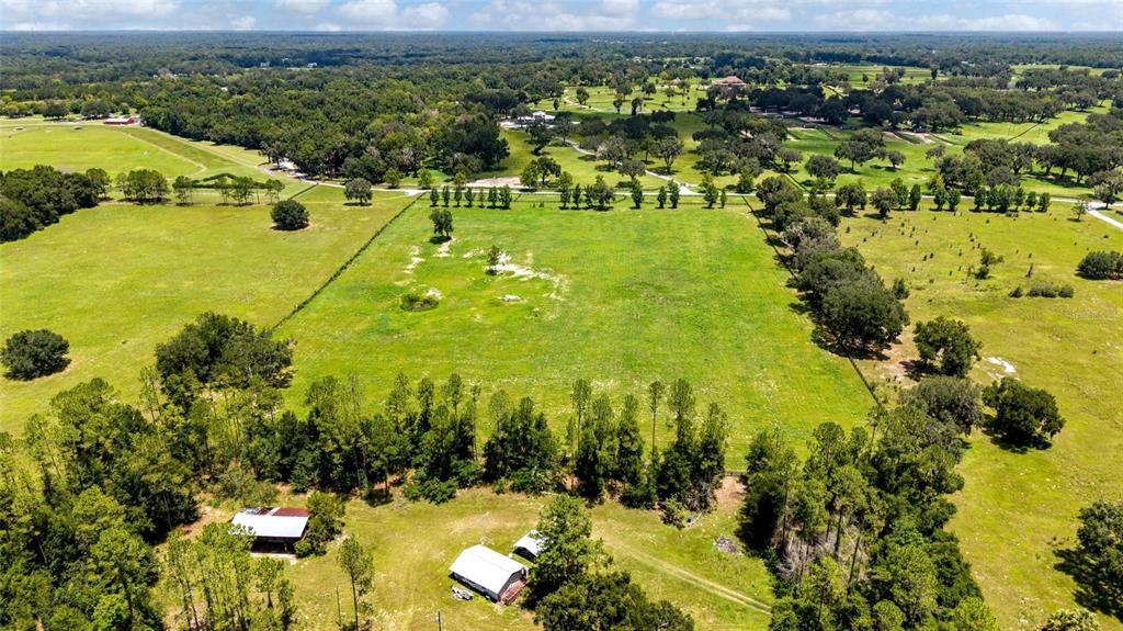 An aerial view shows a large, fenced grassy field surrounded by trees and rural buildings — SE 159TH LN., SUMMERFIELD, FL